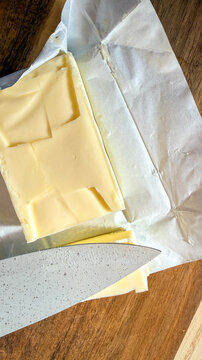 Block of pale butter sliced with a knife on parchment and wooden cutting board in soft natural light, ideal for food blogs recipe pages culinary magazines and social media, 5 May 2026 Subitica, Serbia