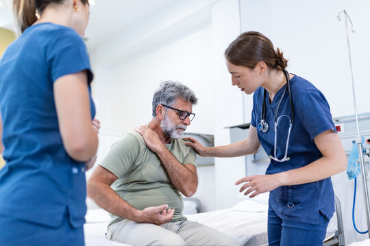 Doctor comforting senior male patient sitting on a hospital bed. Nurse providing empathetic support and care during a consultation. Healthcare, medical support, patient empathy, clinic, wellness.