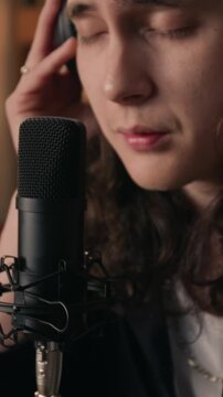 Vertical video of young man wearing headphones and singing into professional microphone. Clip for music production, podcasting, or audio recording school promos