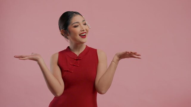 Joyful young Asian woman in a traditional cheongsam qipao dress presenting copy space beside her, isolated by pink background.
