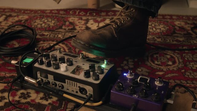 Close-up shot of unknown musician wearing leather boot pressing footswitch on guitar effects pedalboard, changing LED indicator lights. Perfect for music gear reviews, recording studio promos