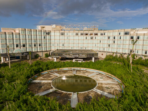 Aerial view of the derelict Tinian Dynasty Hotel with its overgrown courtyard and circular pool, set against a cloudy sky in San Jose, Tinian, Northern Mariana Islands.