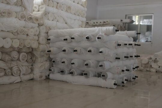 Stacks of large white fabric and textile rolls stored in a factory warehouse for garment production