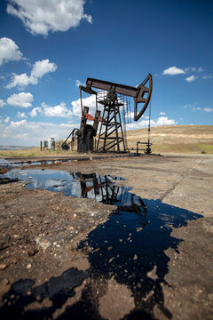 Oil Pumpjack with Crude Oil Reflection in Foreground Under Blue Sky &ndash; Petroleum Extraction and Energy Industry in Rural Landscape