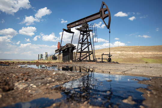 Oil Pumpjack with Crude Oil Reflection in Foreground Under Blue Sky &ndash; Petroleum Extraction and Energy Industry in Rural Landscape