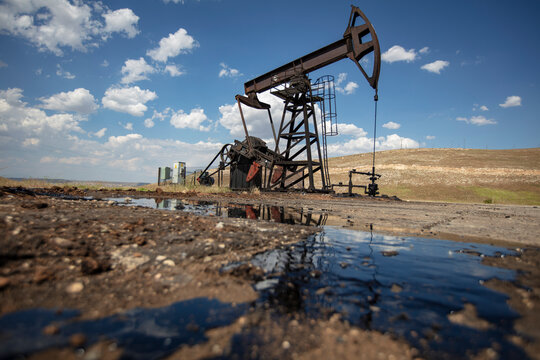 Oil Pumpjack with Crude Oil Reflection in Foreground Under Blue Sky &ndash; Petroleum Extraction and Energy Industry in Rural Landscape