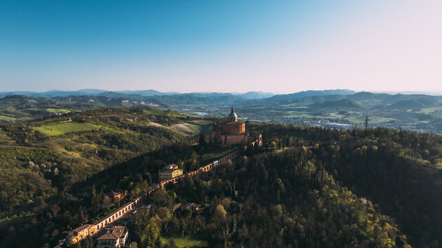Aerial view of the Sanctuary of the Madonna di San Luca perched on a hill, connected by its long portico, surrounded by lush green hills in Bologna, Emilia-Romagna, Italy.