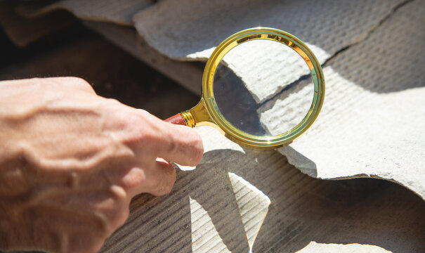 Male hand with a magnifying glass showing old asbestos roof. Health problems