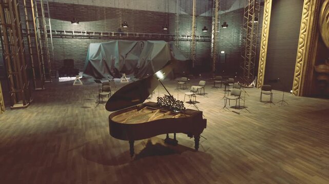 Lonely grand piano on ornate stage, open lid catching warm spotlight empty chairs and scattered microphones suggest recent orchestra rehearsal. Wooden