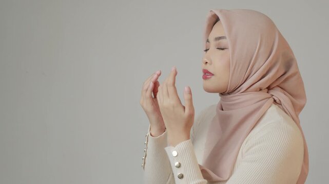 Religious beautiful Asian Muslim girl wearing a headscarf praying to God, isolated by white background.