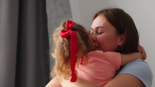 Portrait of caring mother holding and kissing her little girl during a tender family moment indoors. Childhood happiness and emotional connection concept. Celebration of family values and children's w