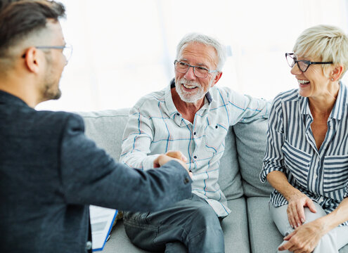 Happy senior old family couple clients make financial insurance estate business deal handshake agent lawyer, satisfied mature customers shake hand meeting bank manager agree on investment contract