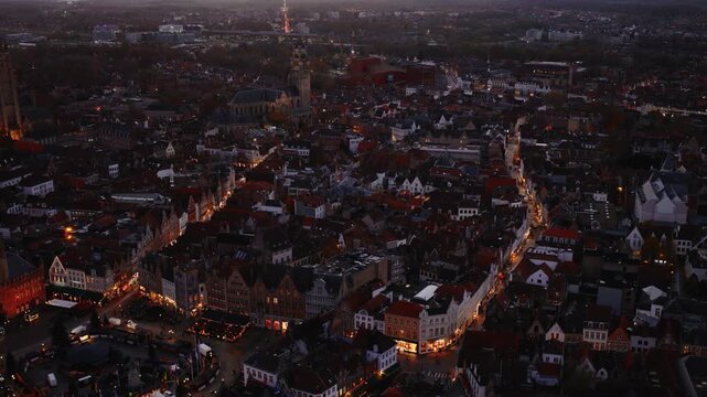 Drone footage showing a part of Bruges city at evening, with warm city lighting, historic buildings, and urban scenery without visible sky.