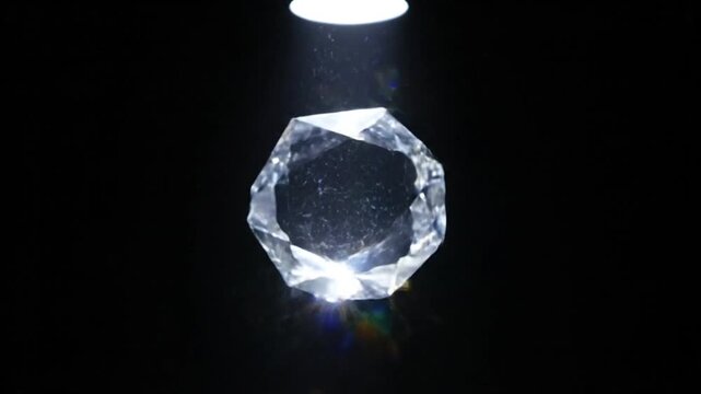 Shimmering faceted crystal gemstone rotating under bright spotlight against dark background.
