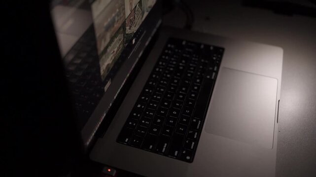 Close-up of hand operating laptop trackpad in low-light home office. Concept of overtime work, focus and modern remote digital workflow.