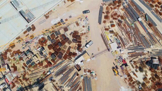 High top-down aerial shot flying over a large construction site with building materials, foundations, and heavy equipment, showcasing the initial stages of a new development project