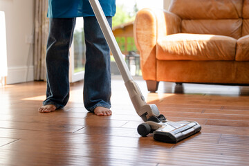Fototapeta premium Person cleans wooden floor using vacuum in living room during daytime with sunlight coming through windows
