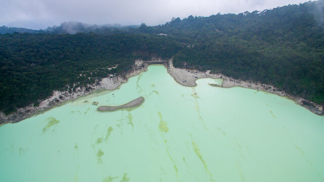 Aerial view of White Crater, a volcanic lake with turquoise waters surrounded by lush green forest and sandy shores in Bandung, West Java, Indonesia.