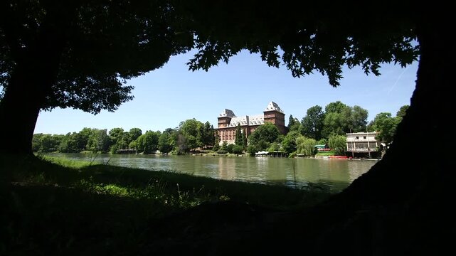 Cinematic slider shot revealing Valentino Castle across the River Po, naturally framed by trees on a sunny day in Turin, Italy