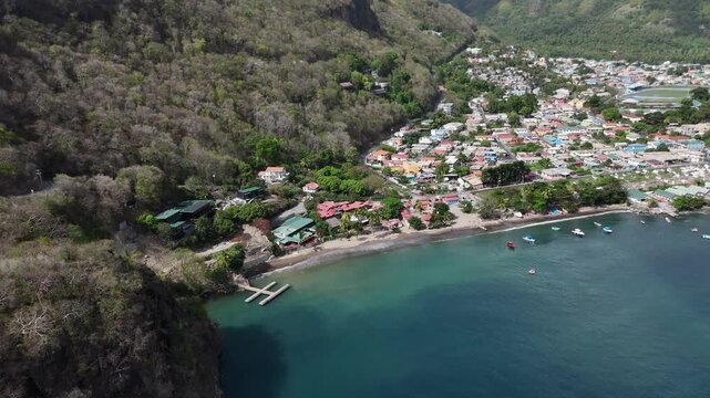 High angle drone perspective of a secluded bay and coastal village surrounded by lush mountains in Saint Lucia, Caribbean