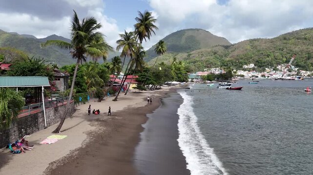 Low altitude drone flight along a sandy tropical beach with palm tree beach bar next to a coastal village in Saint Lucia, Caribbean