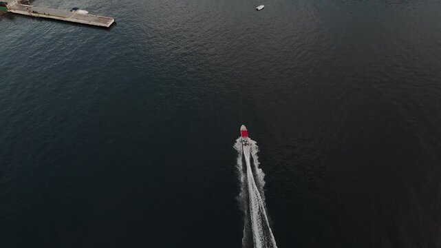 High angle drone tracking shot of a motorboat cruising near the concrete pier and colorful hillside town of Soufriere, Saint Lucia