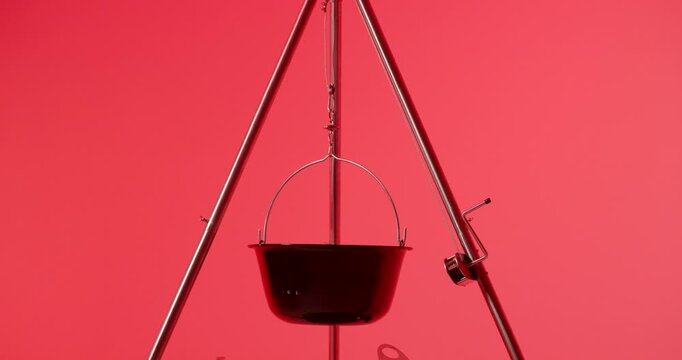 A two tiered circular metal barbecue grill rack hangs from a tripod frame over a metal fire pit