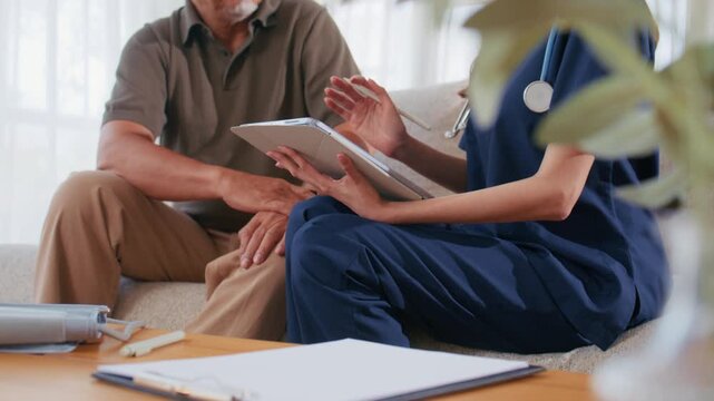 Home Care Scene with Caregiver Discussing Health Concerns and Taking Notes. Female nurse updates a patient record on Tablet during a senior home visit, nursing at home, and home health assessment.