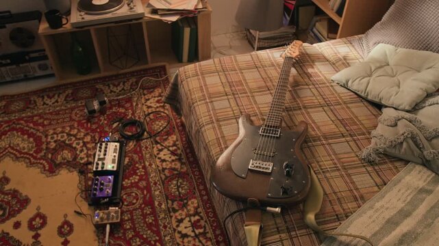 Electric guitar lying on bed next to pedalboard in home studio, camera slowly zooming in. Footage for music education, hobbyist lifestyle branding, or creative industry advertisements