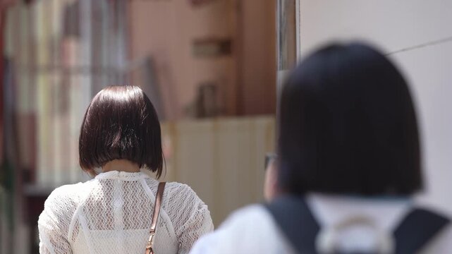 Two people walk side by side, backs to camera. Their movement suggests calm, unhurried pace. Soft focus hints at urban setting or quiet street