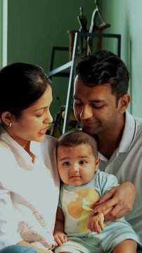 Indian parents and baby boy sitting near bedroom window on cozy bed, mother lovingly points outside, capturing emotional family bonding, modern parenthood, parenting lifestyle, newborn care at home