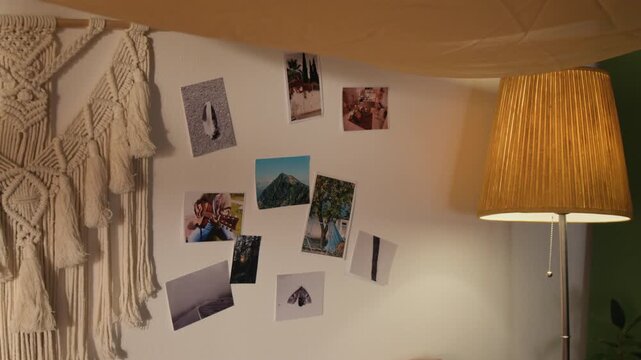 Wall decorated with travel photos, macrame hanging, lit floor lamp. Footage for home decor brands, interior design inspiration, or travel agency advertisements