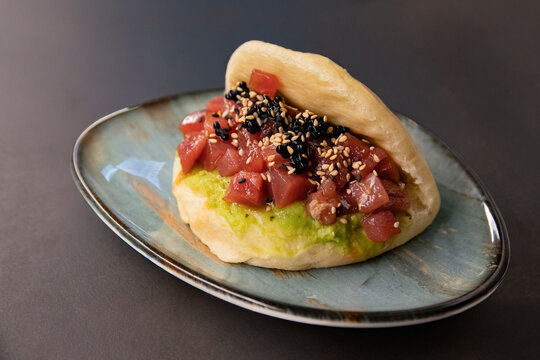 Tuna bao bun with avocado cream sesame seeds and caviar style pearls on plate over dark background