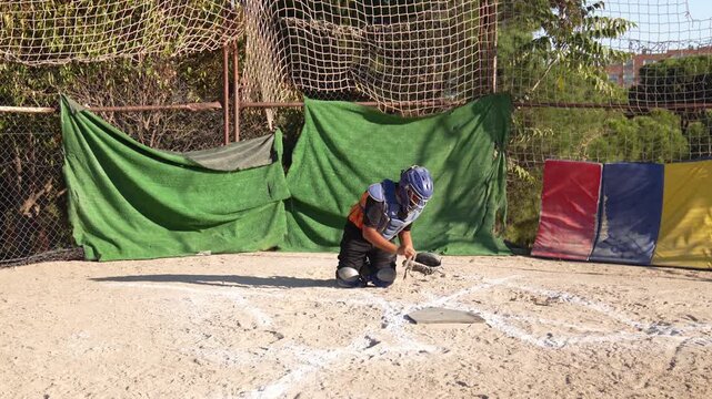 Youth league catcher in full gear successfully catches a baseball during practice. Slow motion footage shows dust flying from his glove