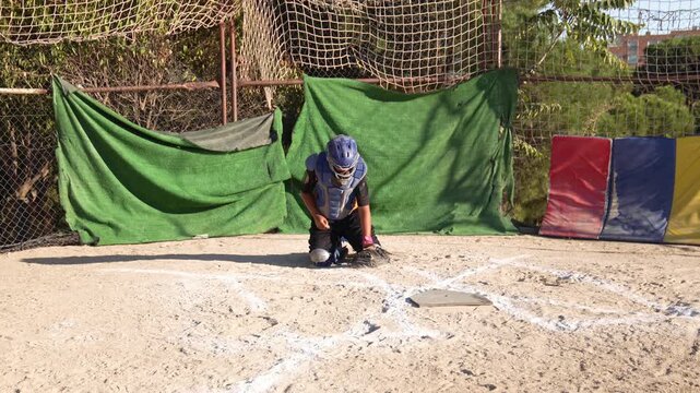 Slow motion of a young catcher in full gear getting into position behind home plate during a youth baseball practice on a sunny day