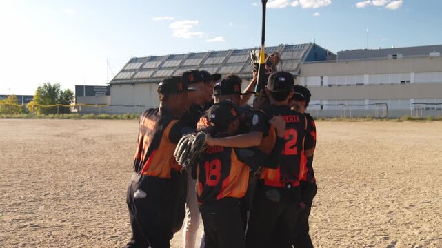 Youth baseball players celebrating victory. The team huddles together, jumping and hugging on the field in a display of teamwork and joy