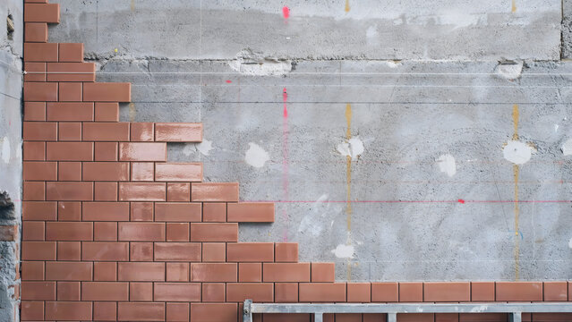 A partially constructed red brick wall against a gray concrete surface