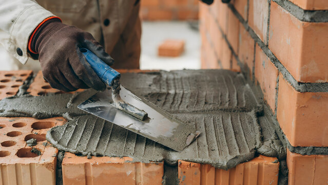 A construction worker spreading wet mortar on red bricks with a steel trowel