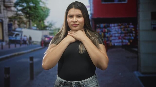 Young woman holds throat with both hands on a city street in front of market stalls and parked vans, eyes closed; panic emergency.