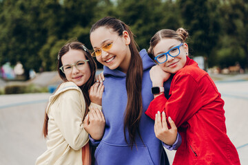 Three teenage girls hugging and smiling outdoors in urban park