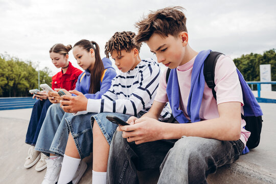 Portrait of teenagers sitting together using mobile phones outdoors