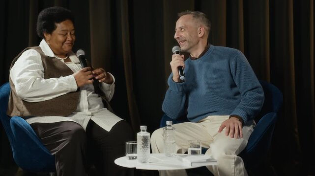 Middle aged Caucasian man and middle aged African American woman speaking into microphones during panel discussion. Clip is ideal for corporate communication and diverse business events