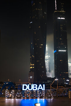 Dubai, UAE - June 16, 2026: Brightly Illuminated Dubai Marina Sign Stands Prominently On Walkway Against Backdrop