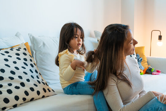 Daughter combing the hair of her mother sitting on the sofa
