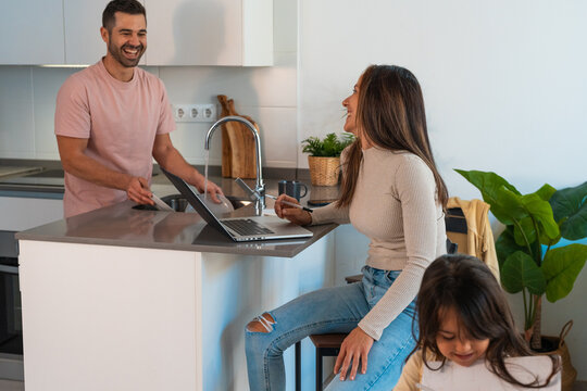 Mother working from home while father cleaning dishes