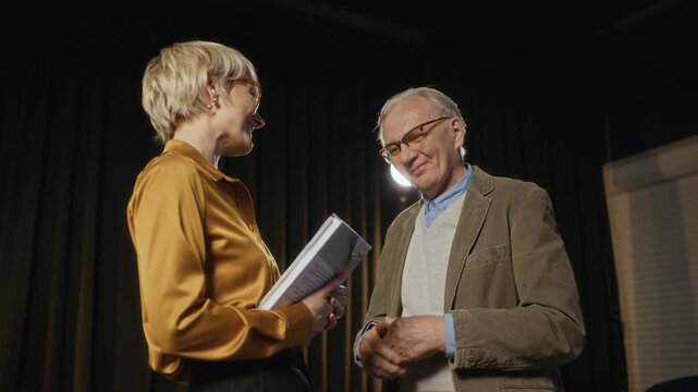 Senior Caucasian man presenting book to middle-aged Caucasian woman on stage during literary event. Footage is ideal for promoting book launches, academic achievements, or library programs, low angle
