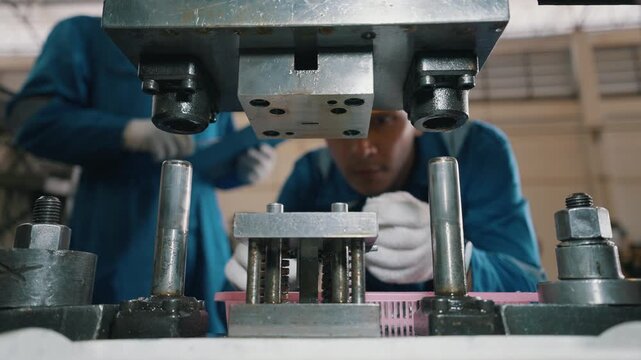 Worker in blue uniform examines metal assembly. Gloved hands adjust precise machine components. Focused expression shows attention to detail. Ideal for manufacturing, industrial, or technical content