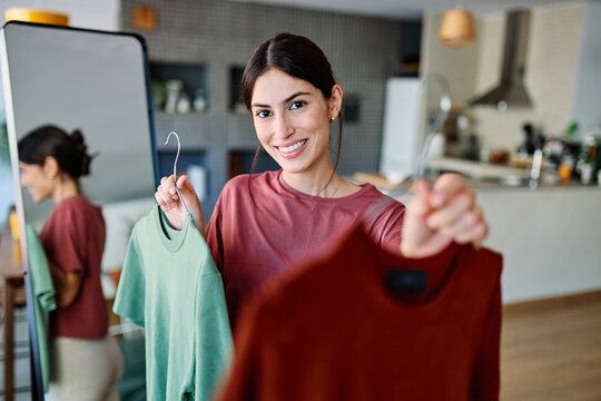 Woman choosing between green and brown shirt in closet in  living room