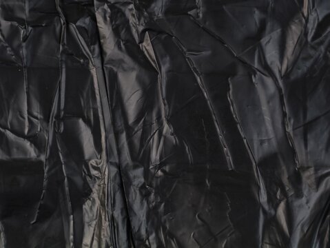 Full frame texture background of a heavily crumpled and wrinkled black plastic sheet, making it an ideal abstract overlay or edgy textured backdrop for modern graphic designs