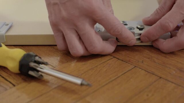 Technician adjusts rollers. Technician calibrates roller adjustment screws precisely. Detailed view of worker adjusting roller screws near screwdriver on wooden patterned surface